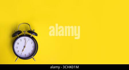 Sveglia nera che mostra sette oclock su sfondo giallo con spazio per le copie. Foto di alta qualità Foto Stock