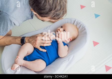 Il padre amorevole interagisce con il suo bambino di 3 mesi che si trova in un accogliente nido di casa. Tenero momento di legame, paternità e connessione precoce in a. Foto Stock