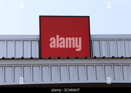 Un vibrante segno rosso bianco montato su un edificio moderno si distingue contro un cielo blu limpido, offrendo un elemento di design minimalista perfetto per vari noi Foto Stock
