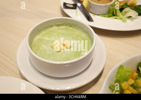 Zuppa di spinaci verdi in una ciotola bianca con un piattino sul tavolo da pranzo. E c'era un'insalata di tonno su un piatto bianco nelle vicinanze. Foto Stock