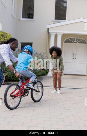 Genitori afroamericani che insegnano ai bambini di andare in bicicletta davanti a casa Foto Stock