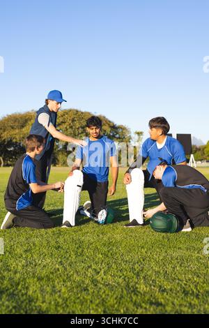 Squadra maschile di cricket con maglie blu che legano i pattini alle gambe con i ceppi e i caschi sul campo di cricket Foto Stock