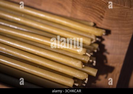 sottili candele di cera d'api gialle disposte ordinatamente in un recipiente di legno. La profondità di campo ridotta crea uno sfondo morbido e sfocato, che mette a fuoco l'smo Foto Stock