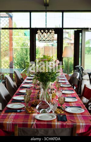 Un tavolo da pranzo splendidamente allestito adornato da un vibrante pezzo centrale floreale. la tovaglia a quadri rossa aggiunge un tocco di eleganza, perfetta per riunioni e incontri Foto Stock