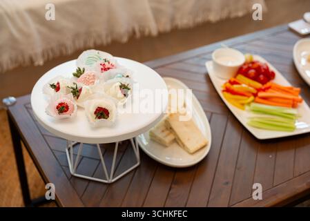 Un tavolo splendidamente organizzato presenta dessert decorativi su un banco bianco e un variopinto assortimento di verdure e salse su una superficie di legno, pervade Foto Stock