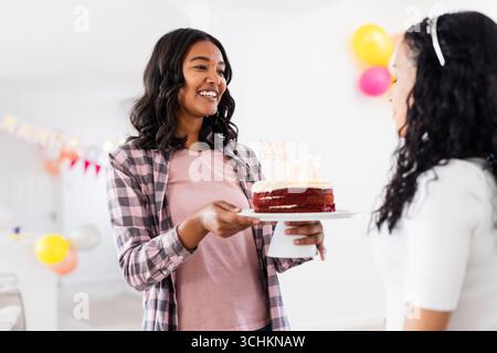 Donna sorridente che tiene la torta di compleanno, festeggia a casa con la famiglia e diverse amiche Foto Stock