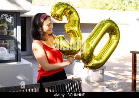 Alla festa, donna che tiene in mano palloncini d'oro per celebrare il 30° compleanno sul ponte, sorridendo con gioia Foto Stock