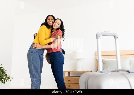 Diverse amiche che abbracciano in camera da letto con la valigia, esprimono amicizia, a casa, spazio copia Foto Stock