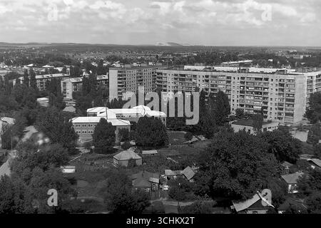 Una fotografia d'archivio in bianco e nero scattata nella città di Sloviansk nel luglio 1997. Una vista panoramica ad alto angolo dal quartiere Svobody. La cornice mostra un'area residenziale con edifici standard a nove piani, una scuola e un settore residenziale privato. Un cumulo di scorie (terrikon) è visibile all'orizzonte, sottolineando il carattere industriale di Sloviansk. Il paesaggio riflette l'eredità dell'era sovietica negli anni '1990 Foto Stock