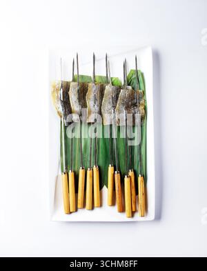 Spiedini di pesce ago su piatto rivestito di foglie Foto Stock