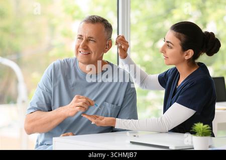 Uomo maturo con l'apparecchio acustico visita medico al tavolo in clinica Foto Stock