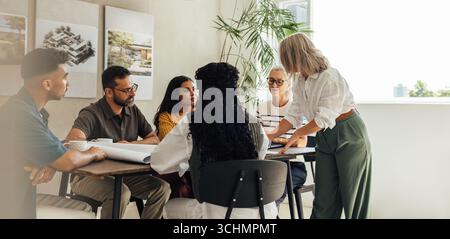 Un gruppo di architetti che collaborano in un ufficio moderno. Il team eterogeneo, con uomini e donne di varie età, discute i progetti e i piani in una pr Foto Stock