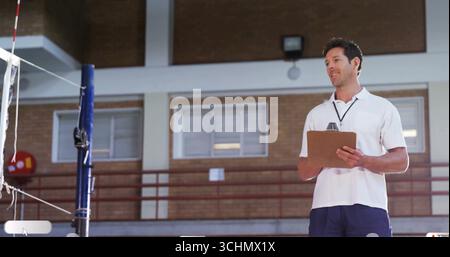 Allenatore in piedi con appunti, fischio in palestra con rete da pallavolo, stand, spazio per fotocopie Foto Stock