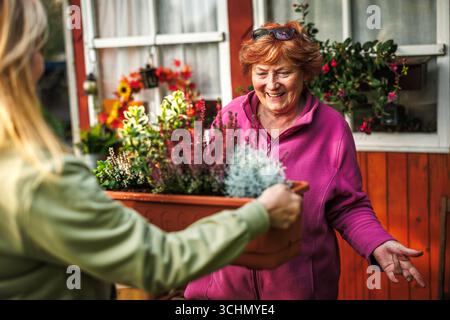 Giardinaggio autunnale. Felice donna anziana sorridente e sua figlia adulta che piantano fiori, celebrando il loro legame e la gioia di passare del tempo insieme all'aria aperta Foto Stock