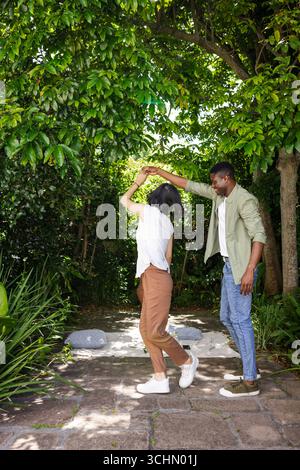 Coppia che balla gioiosamente sotto lussureggianti alberi verdi in giardino, celebrando l'amore Foto Stock