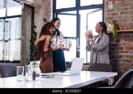 Celebrando il successo, diverse colleghe applaudono e abbracciano in un ufficio moderno Foto Stock