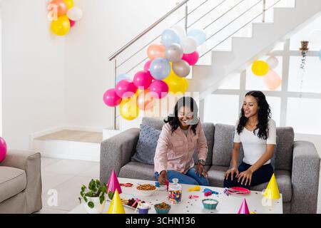 Festeggiando a casa, due amiche diverse si godono le colorate decorazioni delle feste di compleanno Foto Stock