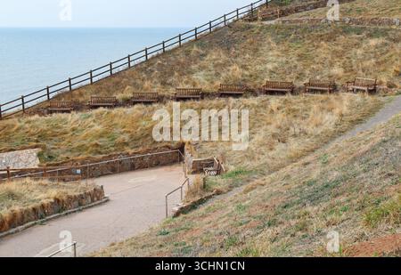 Fila di vecchie panchine in legno con vista mare a Sidmouth, Devon orientale Foto Stock
