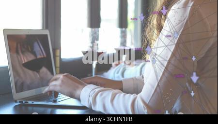 Donna con camicetta bianca che scrive su un laptop in un bar, con bicchieri da vino, candelabri, grafica di rete Foto Stock