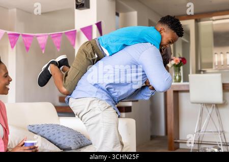 Padre che gioca con il figlio sul retro in salotto, madre sorridente nelle vicinanze Foto Stock