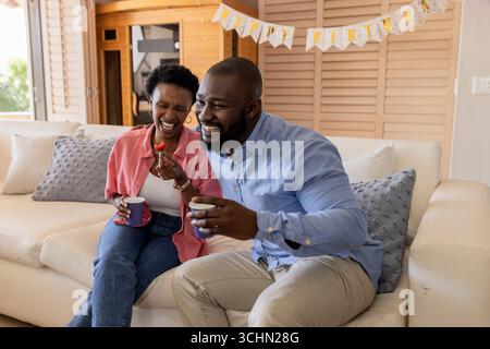Festeggiamo il compleanno, la coppia felice si gusta un caffè e si ride su un comodo divano Foto Stock