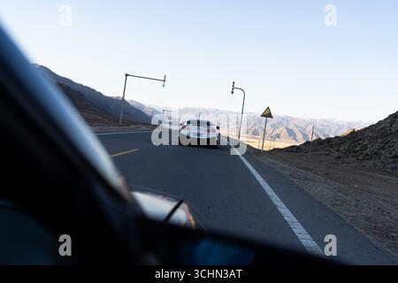 Un'auto sportiva bianca che precede su un'autostrada asfaltata, catturata attraverso il finestrino laterale di un altro veicolo. Foto Stock