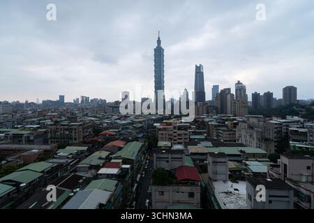 Vista ad alto angolo del paesaggio urbano di Taipei, con l'iconica torre Taipei 101 che si innalza sopra i tetti densi sotto un cielo nuvoloso. Foto Stock