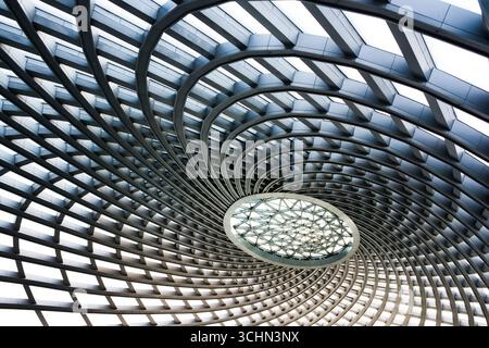 Vista ad angolo basso di un dinamico soffitto a reticolo in metallo con lucernario geometrico centrale. Foto Stock