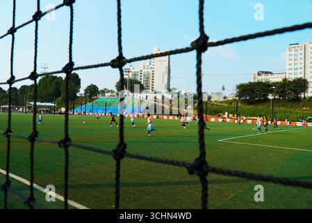 Bambini coreani che giocano a calcio (calcio) su un campo artificiale con i genitori che guardano Foto Stock