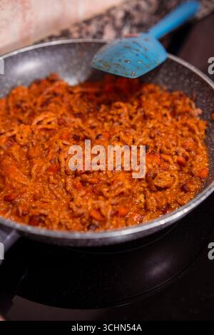 Tritare la carne con le carote tritate e la salsa di pomodoro fatta in casa cucinando sulla padella su una stufa a induzione. Cottura di un piatto delizioso con carne macinata fresca. Foto Stock