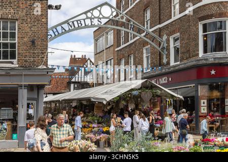 Shambles Market a York, in Inghilterra, con bancarelle di fiori e folle di acquirenti sotto il tetto, creando una vivace scena di commercio e comunità locale. Foto Stock