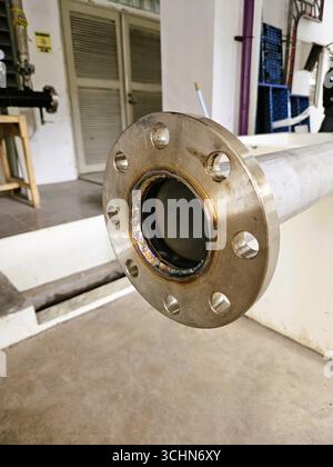 Primo piano della flangia del tubo metallico in un impianto industriale, parte di un sistema meccanico per il collegamento dei fluidi Foto Stock