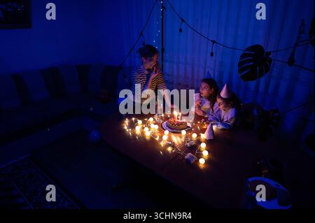 Un accogliente soggiorno si anima di candele accese e risate mentre gli amici festeggiano un compleanno di notte, circondati da dolci e decorazioni per feste Foto Stock