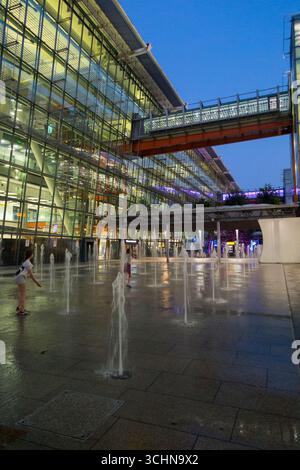 Fontane d'acqua con alcuni bambini/bambini che giocano al crepuscolo mentre la notte scende fuori dalla sala d'ingresso del terminal 5 dell'aeroporto di Londra Heathrow. Londra. REGNO UNITO. (145) Foto Stock