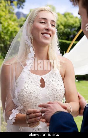 Sposa sorridente mentre si scambiano i voti durante la cerimonia di nozze all'aperto Foto Stock