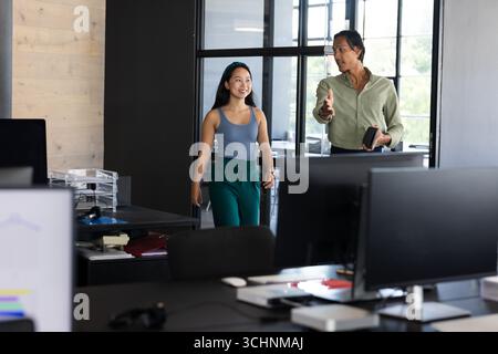 Discutere del progetto, diversi colleghi che camminano attraverso un ufficio moderno, sorridenti e impegnati Foto Stock