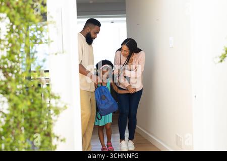 Genitori che aiutano la figlia con lo zaino, si preparano per la scuola in corridoio Foto Stock