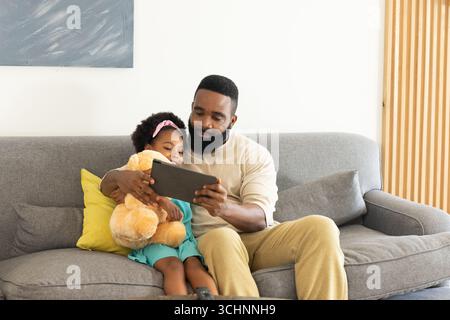Padre e figlia seduti sul divano con un tablet, godendosi momenti di qualità insieme Foto Stock