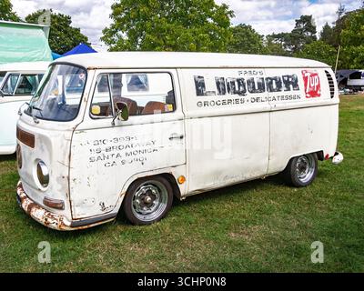 Pulmino Volkswagen bianco d'epoca con segnaletica retrò parcheggiato sull'erba durante un evento all'aperto in una giornata di sole Foto Stock