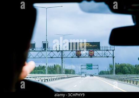 Mosca, Russia, 18.08.2025 uomo che guida un'auto su un'autostrada, guardando i cartelli stradali elettronici con limite di velocità e messaggio di sicurezza. Concetto di controllo del traffico Foto Stock