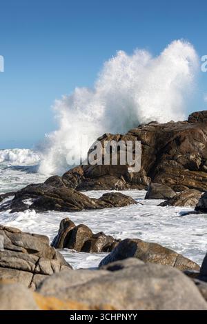 Big Ocean Wave che si schianta contro Rock con spettacolare Splash che mostra il potere del mare sotto cieli azzurri e coste rocciose Foto Stock