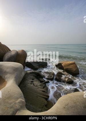 Onde schiumose che si lavano su rocce di arenaria erose sulla costa del Golfo Persico dell'Iran meridionale. Foto Stock