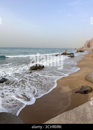 Spiaggia di sabbia dorata e dolci onde con rocce sparse lungo il Golfo Persico nel sud dell'Iran. Foto Stock
