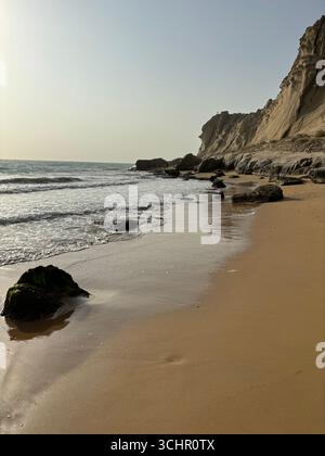 Spiaggia di sabbia dorata con rocce sparse e torreggianti scogliere di arenaria lungo la costa del Golfo Persico nel sud dell'Iran. Foto Stock