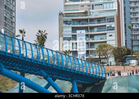 Lima perù agosto 30 2025: Persone che attraversano il nuovo ponte blu villena rey a miraflores, lima, con uno striscione di protesta appeso a un edificio vicino Foto Stock