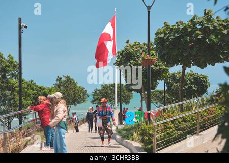 Lima perù agosto 30 2025: Turisti che si godono una giornata di sole a miraflores, lima, con la bandiera peruviana e la vista sull'oceano pacifico nel nuovo parco del ponte Foto Stock