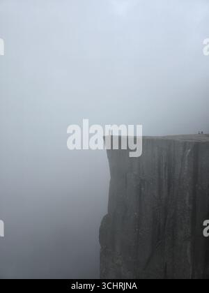 La maestosa scogliera di Preikestolen si innalza drammaticamente sopra i fiordi della Norvegia, offrendo vedute mozzafiato. Gli avventurieri si stagliano sul bordo, avvolti da una misteriosa nebbia, creando un'atmosfera maestosa. Foto Stock
