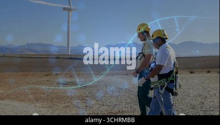 Cammina due tecnici in attrezzatura di sicurezza gialla che attraversano il parco eolico, sovrapposizione dell'elica del DNA, spazio di copia Foto Stock
