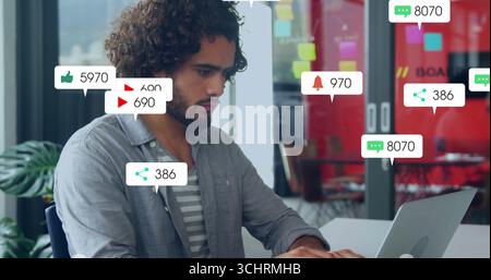 Un uomo dai capelli ricci che scrive sul laptop in un ufficio moderno, con icone di notifica e spazio di copia Foto Stock