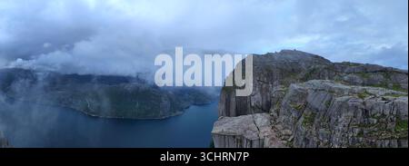 La scogliera mozzafiato di Preikestolen si innalza drammaticamente sopra le tranquille acque di Lysefjorden, circondata da una splendida bellezza naturale e avvolta dalla nebbia. Un posto perfetto per gli amanti dell'avventura. Foto Stock